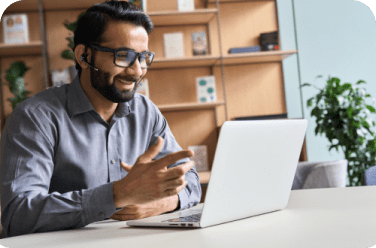 Un colaborador joven, seguro de sí mismo y sonriente, trabaja con su laptop sobre el escritorio de una oficina. 