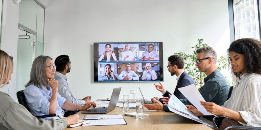 Un grupo de colaboradores se encuentran conectados a una videollamada adentro de una sala de reuniones. En la pantalla LED se visualizan 6 personas conectadas a distancia. 