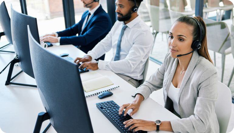 Un equipo de agentes de centro de contacto operan en un día cotidiano en su centro de trabajo. Tienen computadoras y diademas para atender llamadas. 