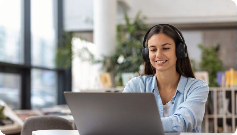 Una universitaria utiliza una laptop y audífonos de diadema para aprender en línea en el interior de una biblioteca 