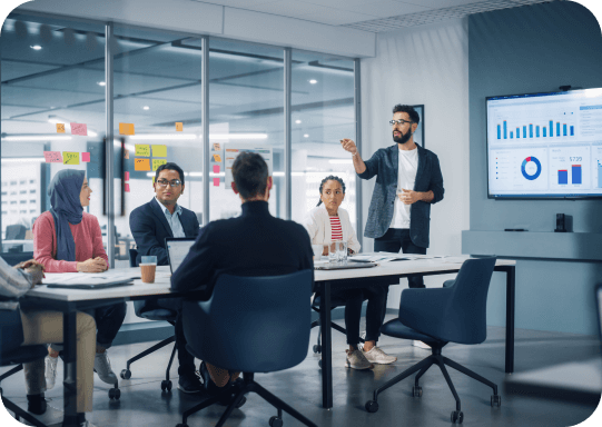 Un equipo de colaboradores analiza unas gráficas en una pantalla led gigante, mientras uno de ellos expone. Todos se encuentran en el interior de una sala de juntas. 