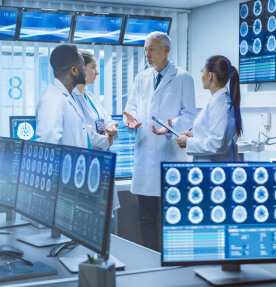 Un grupo de doctores conversan en una sala de alto equipamiento tecnológico. Muchos monitores visualizan radiografías digitales. 