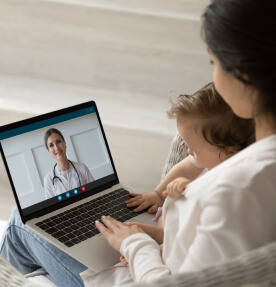 Una madre joven y su pequeño hijo tienen una videollamada con una médico desde una laptop. 