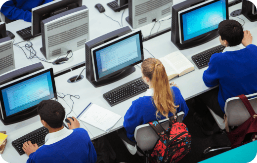 Imagen en picada, mostrando un salón de cómputo donde 3 estudiantes realizan actividades en computadoras de escritorio. 